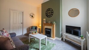 A living room with a fireplace, a television on a stand, a sofa, and a coffee table. - The Alfred Suite | Redcar (Redcar and Cleveland)