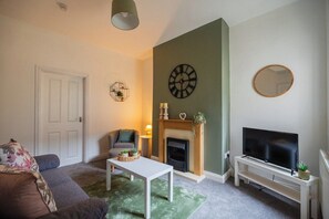 A living room with a fireplace, a television on a stand, a sofa, and a coffee table. - The Alfred Suite | Redcar (Redcar and Cleveland)