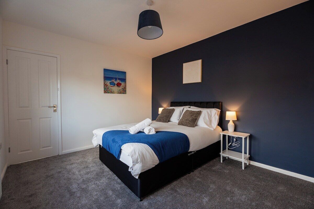 A bedroom with a bed, a bedside table with a lamp, a door, and a wall with a painting.