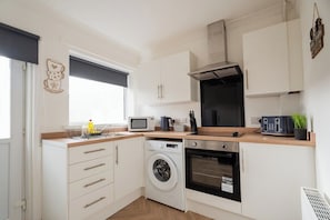 A compact kitchen with a washing machine, oven, microwave, and toaster. - 3BR Barnaby House | Contractor Friendly | Sleeps 5 (Redcar and Cleveland)