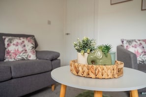 A living room with a grey sofa, a round table with a woven tray, and two potted plants. - Stunning Laburnum House | 4BR | Parking | Sleeps 7 (Redcar and Cleveland)