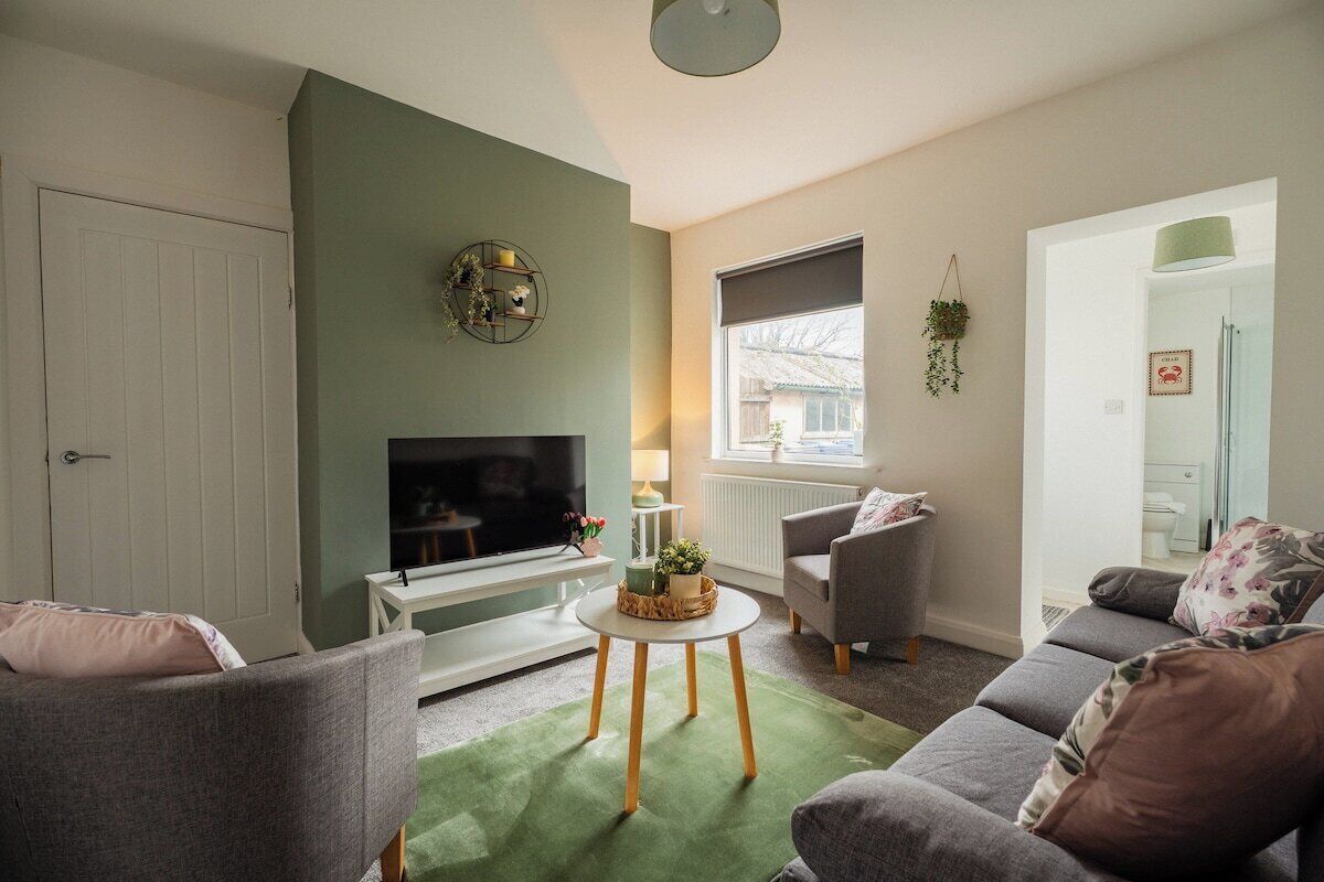 A living room with a flat-screen TV, a sofa, a coffee table, and a window with a view of the outside.