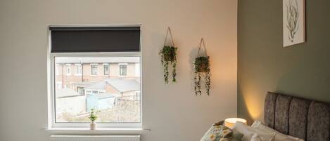 A bedroom with a bed, a window, a radiator, and hanging plants.