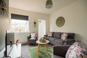 A living room with a sofa, armchairs, a coffee table, a television, and a wall clock. - Stunning Laburnum House | 4BR | Parking | Sleeps 7 (Redcar and Cleveland)