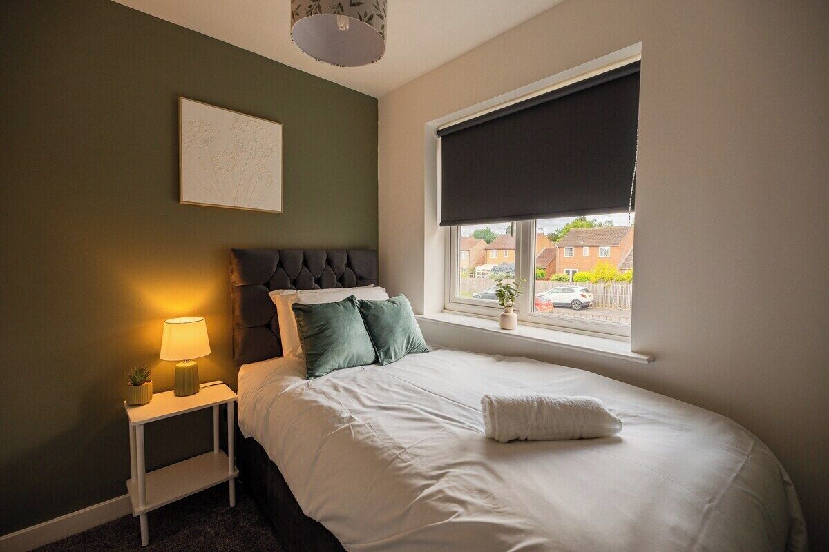 Een slaapkamer met een bed, nachtkastje, lamp en een raam met uitzicht.
