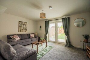 A living room with a grey sofa, a wooden coffee table, and a green rug. - 3BR Einstein House in Hardwick | Work Friendly (Stockton-on-Tees)