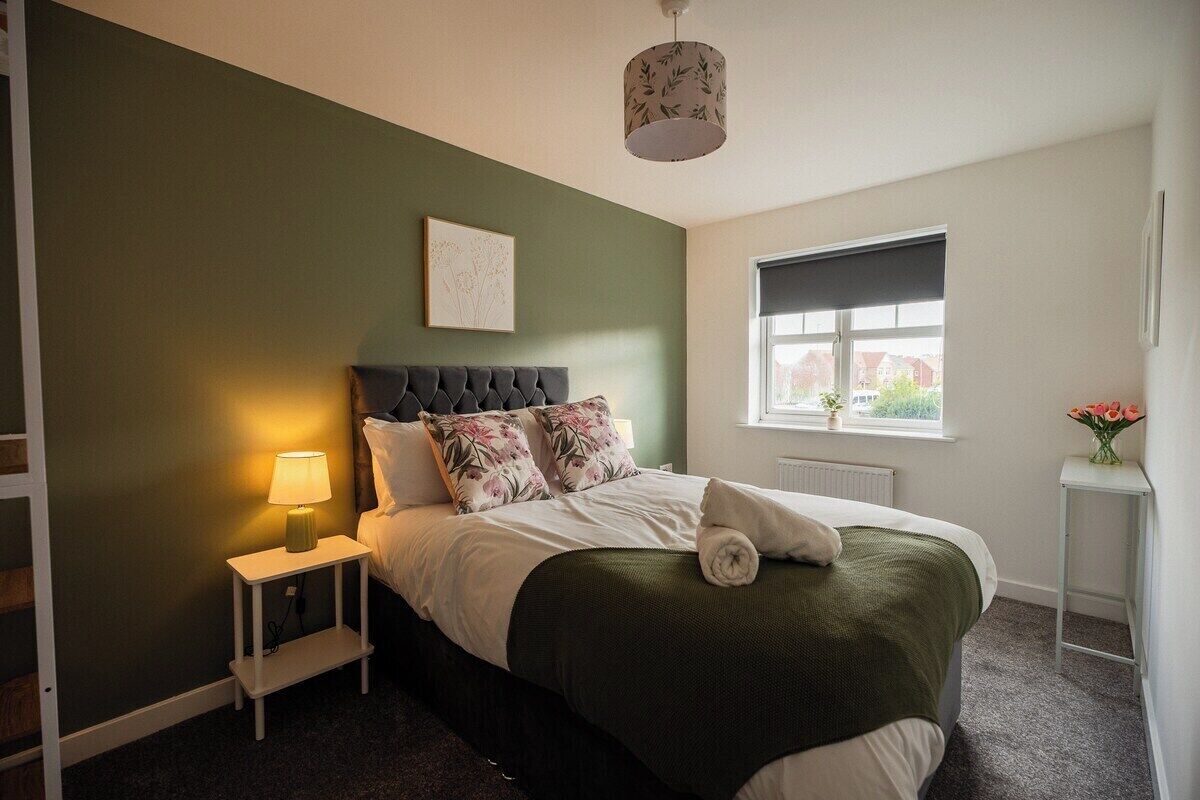 Een slaapkamer met een bed, nachtkastje, lamp, raam en uitzicht.