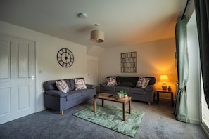 A living room with two sofas, a coffee table, a wall clock, a lamp, and a window with curtains. - 3BR Einstein House in Hardwick | Work Friendly (Stockton-on-Tees)