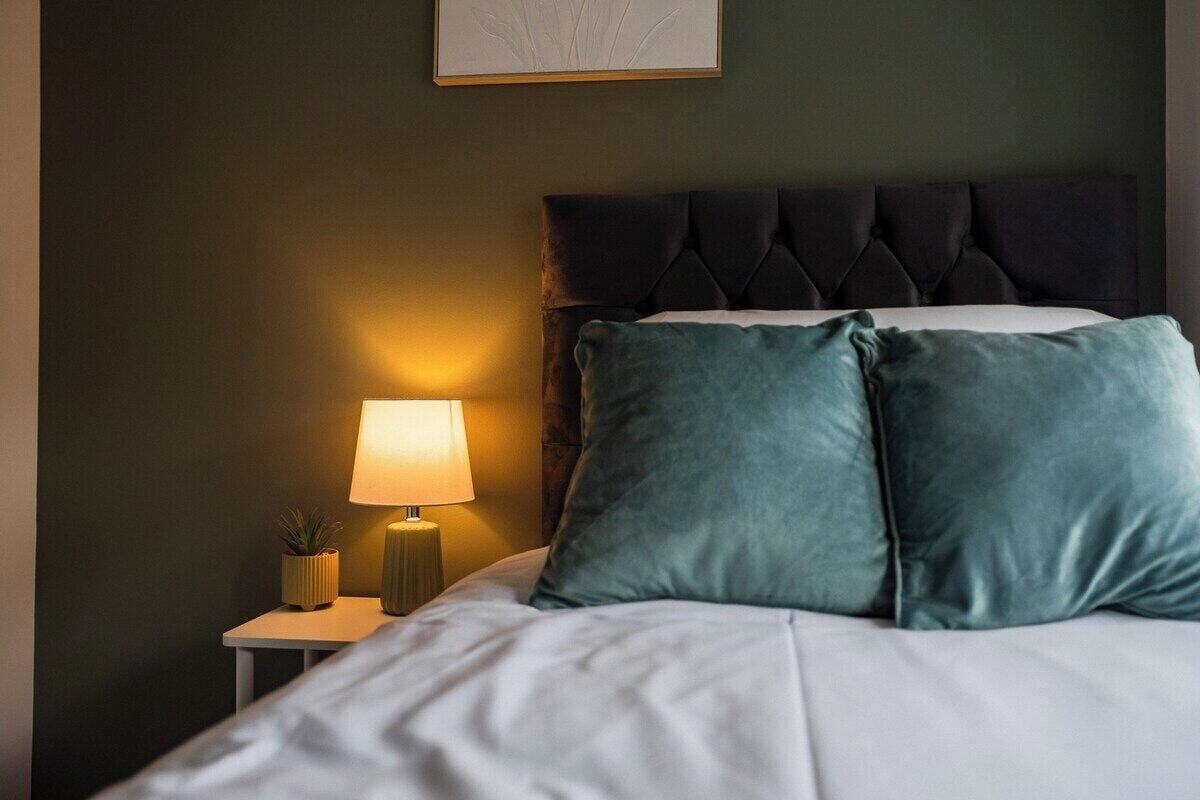 A neatly made bed with two pillows, a bedside lamp, and a small plant on a nightstand.