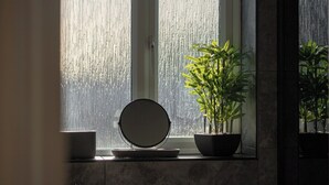 Uma casa de banho com uma janela grande, um espelho redondo e uma planta em vaso.