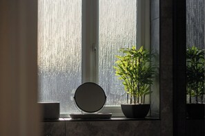 Ein Badezimmer mit einem großen Fenster, einem runden Spiegel und einem Blumentopf.