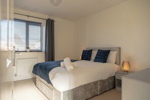 Een slaapkamer met een bed, nachtkastje, lamp en raam met gordijnen.