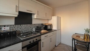 Uma cozinha compacta com fogão a gás, micro-ondas e uma pequena mesa de jantar com uma planta.