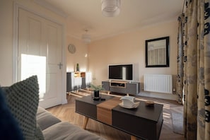 Ein modernes Wohnzimmer mit Sofa, Couchtisch, Fernseher und Heizkörper.