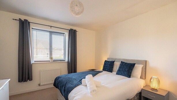 Quarto de hotel com cama, mesa de cabeceira, luminária e janela com cortinas.