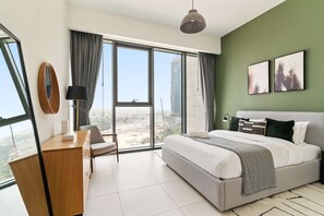 A modern bedroom with a large bed, a desk, a chair, a lamp, and a view of a cityscape through large windows. - Silkhaus City View 3BR Nearby Canal in Al Wasl (Dubai)