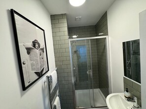 A bathroom with a glass shower enclosure, a sink, and a framed picture on the wall. - Modern 6 Bed Stay in Hartlepool | Work friendly (Hartlepool)