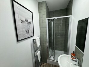 Ein Badezimmer mit einer Duschkabine, einem weißen Waschbecken und einem gerahmten Bild an der Wand.
