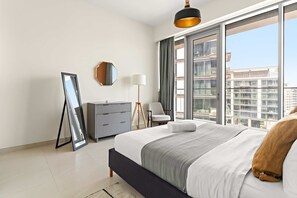 Ein modernes Schlafzimmer mit einem großen Bett, einer Kommode, einem Spiegel, einer Lampe und Blick auf die Stadt durch große Fenster.