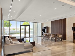 Eine geräumige Lobby mit einem modernen Sofa, einem Essbereich und großen Fenstern mit Blick ins Freie.