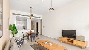 A modern living room with a sofa, coffee table, TV, and a dining area with chairs and a table. - Silkhaus Premium 2bdr Stay in Canal Front (Dubai)