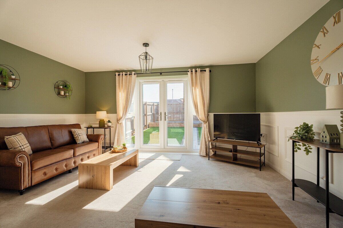 A living room with a sofa, coffee table, TV stand, and a large window with curtains.