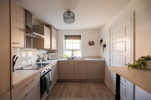 A compact kitchen with a microwave, stove, and sink. There is a window with a view of the outdoors. - 3BR Norton Nook | Sleeps 5 | Work Friendly + WiFi (Stockton-on-Tees)
