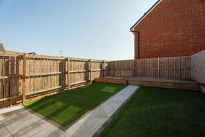 A backyard with a wooden fence, a brick building, and a well-maintained lawn. - The Norton Nook | Horizon Stays (Stockton-on-Tees)