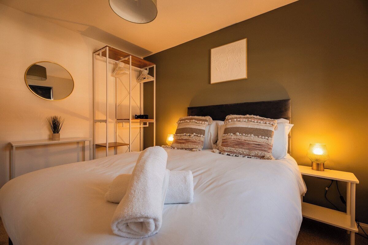 A neatly made bed with rolled towels, a bedside lamp, and a wall-mounted mirror.