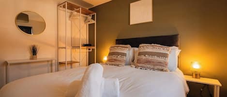 A neatly made bed with rolled towels, a bedside lamp, and a wall-mounted mirror.