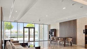 A spacious lobby with a modern sofa, a dining area, and large windows offering a view of the outdoors. - Silkhaus Contemporary 2BR Canal View Stay (Dubai)