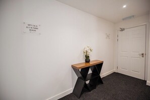A hallway with a sign indicating the location of the laundry room, a small table with a vase of flowers, and a door. - 1 Bedroom Studio Apartment ~ Central Middlesbrough (Middlesbrough)