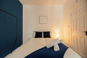A hotel room with a bed, a bedside lamp, a framed picture on the wall, and a door. - 1 Bedroom Studio Apartment ~ Central Middlesbrough (Middlesbrough)