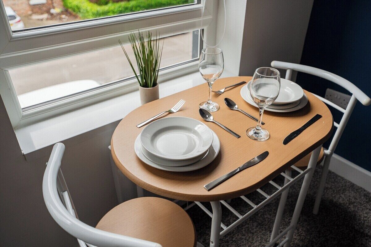 Een eettafel gedekt met borden, bestek en glazen, vlakbij een raam met uitzicht op groen.