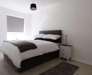 Een moderne slaapkamer met een bed, nachtkastjes, een lamp en een raam.