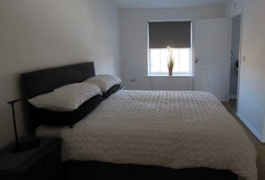 Ein Schlafzimmer mit Bett, Nachttisch, Fenster und Tür.