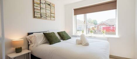 Un dormitorio con cama, mesita de noche, lámpara, ventana con vistas y una obra de arte colgada en la pared.