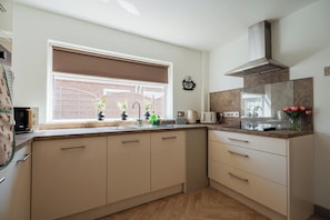A modern kitchen with a window, built-in cabinets, a stainless steel range hood, and a countertop with various appliances. - Stylish 3BR Bungalow with Garden | Sleeps 6 (Redcar and Cleveland)