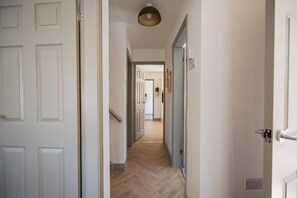 A hallway with a wooden floor, white walls, and a door at the end. - Stylish 3BR Bungalow with Garden | Sleeps 6 (Redcar and Cleveland)