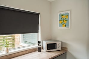 A kitchen with a microwave on the counter, a window with a blind, and a poster on the wall. - 4BR Humber House for 7|Contractor Stay|Thornaby (Thornaby)