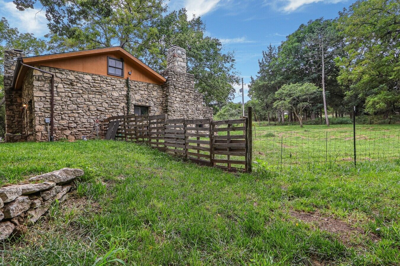 A stone building with a wooden door, surrounded by a grassy field and trees.