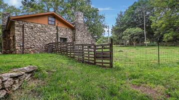 A stone building with a wooden door, surrounded by a grassy field and trees.