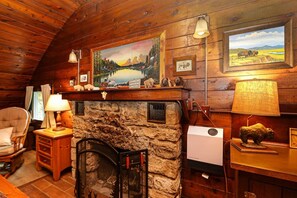 A cozy cabin interior with a stone fireplace, wooden walls, and various decorative items including animal figurines and framed pictures.
