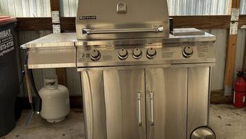A stainless steel Jenn-Air gas range with four burners and a griddle, located in a garage with a corrugated metal wall and a concrete floor.