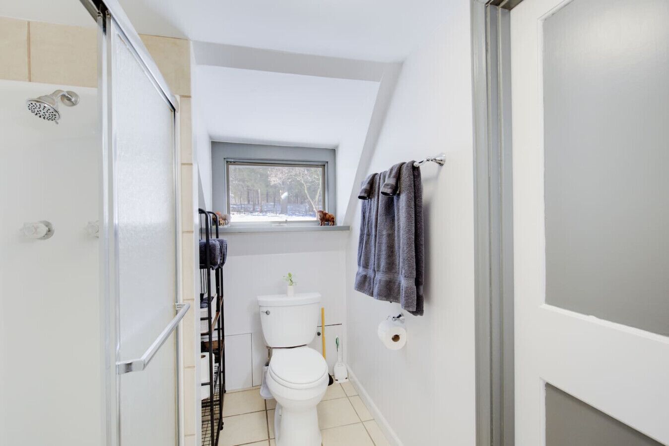 Une petite salle de bain comprenant une douche, des toilettes et une petite fenêtre.