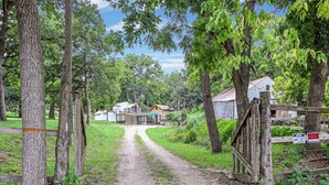 A rural path leading to a cluster of buildings surrounded by trees.