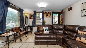A living room with a brown leather sofa, a wooden table, and a window with curtains.