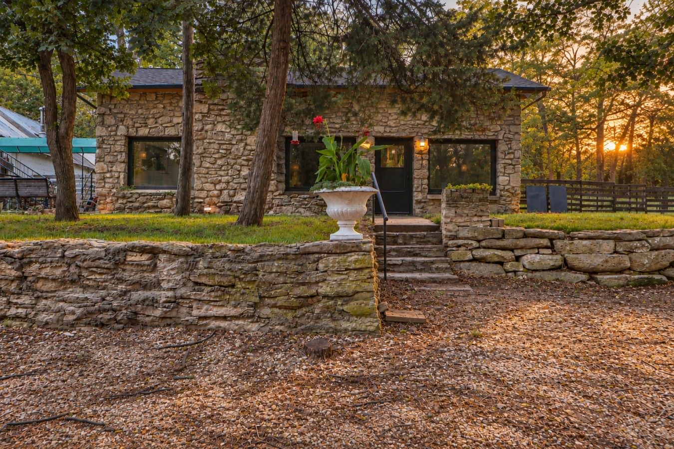 A stone building with a stone wall entrance, a large planter with a plant, and a bench.