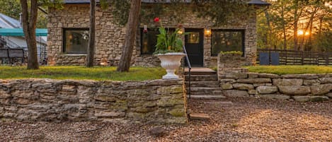 A stone building with a stone wall entrance, a large planter with a plant, and a bench.