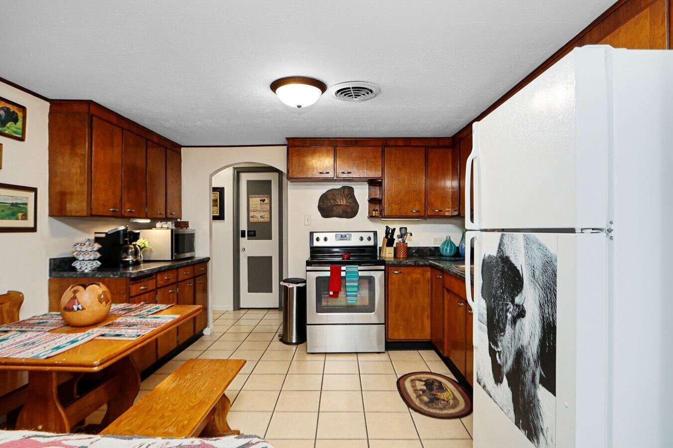 A kitchen with wooden cabinets, a stove, a refrigerator, and a dining table with chairs.
